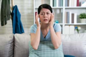 Young woman sitting on couch, holding fingers to forehead, looking distressed