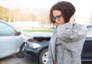Woman holding the back of her neck, car crash in background
