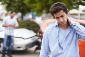 Young man rubbing back of neck in pain, car crash in background