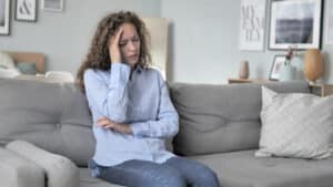 Distressed woman holding hand to head, sitting on couch