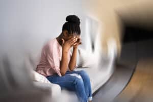 Young woman sitting on couch holdng hands to head, image blurred around her