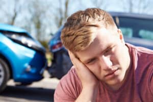 Young man resting head in hands, looking stressed, car accident in background